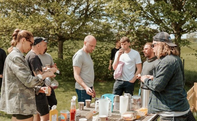 Föräldrar samlade kring ett bord med drycker och förnödenheter utomhus.