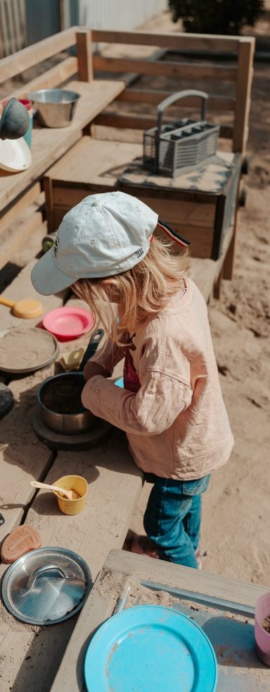 Litet barn leker med sand vid en lekstation utomhus.